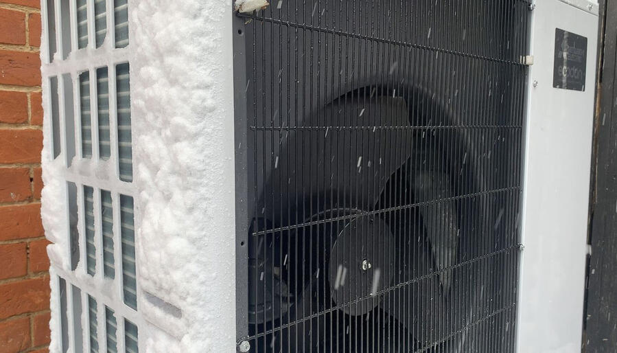 Air source heat pump outdoor unit working in the snow